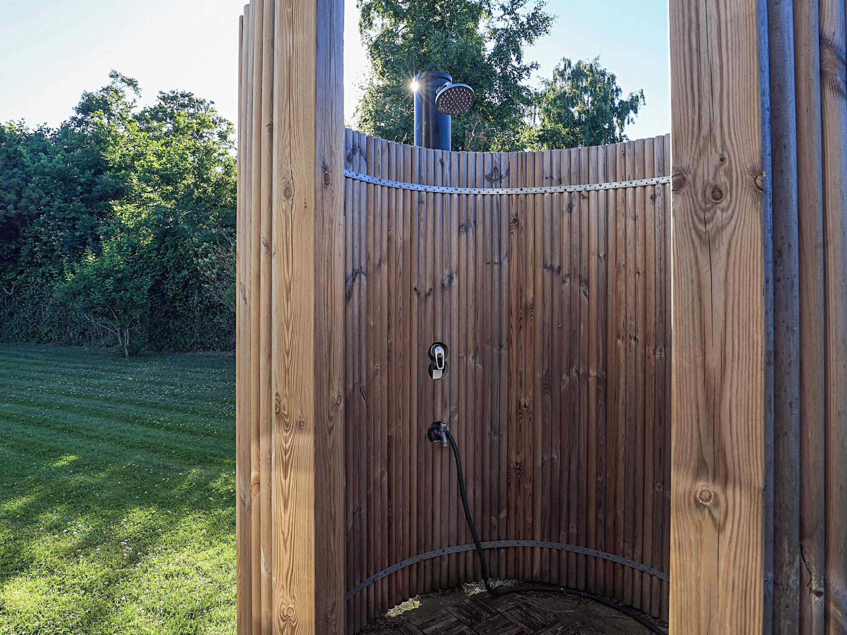 A wooden outdoor shower enclosure with a metal frame, a hose, and a showerhead.