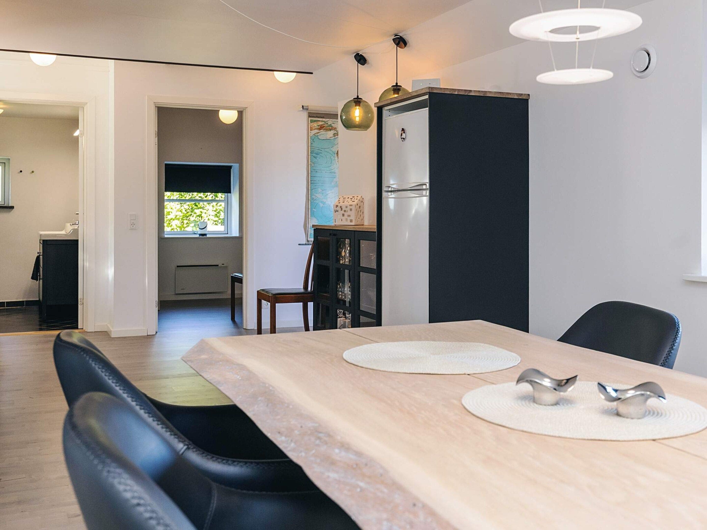 Eine moderne Küche mit einem eingebauten Kühlschrank, einem Esstisch mit Unterlagen und Blick ins Freie durch ein Fenster.