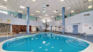 Una piscina interior con indicador de profundidad de 3 pies, rodeada de paredes con señales de seguridad, un tramo de pared de piedra y una escalera que lleva a un nivel superior.