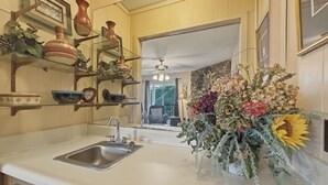 Una cocina con un lavamanos, repisas con cerámica y un gran arreglo floral.