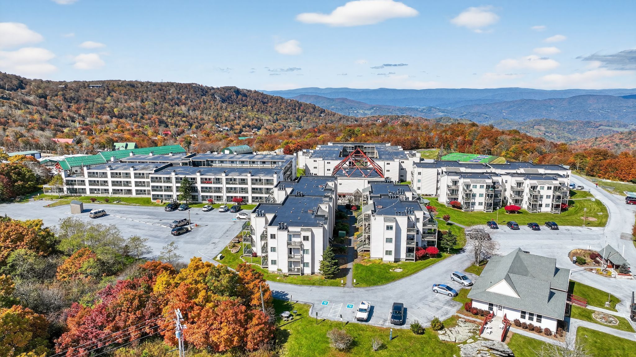 A multi-story hotel with a parking lot, surrounded by autumn foliage and mountains.