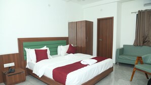 A neatly arranged bedroom with a bed, a green sofa, a wardrobe, and a nightstand with a phone. - Hotel Akash Palace  (Kotda Sangani)