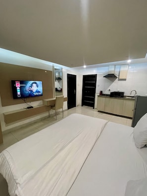A modern hotel room with a bed, a TV, a small kitchenette, and a bathroom. - YP George (Lekki)
