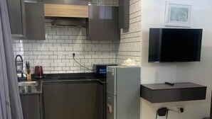 Una cucina compatta con frigorifero, forno a microonde e TV a schermo piatto montata a parete.
