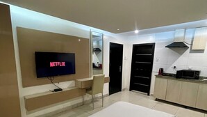 Una camera moderna con un letto grande, una TV a parete, una scrivania e un angolo cottura con pensili e un forno a microonde.