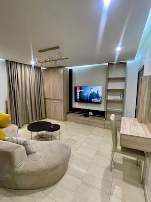 A modern living room with a flat-screen TV, a sofa, a coffee table, a dining area, and a built-in shelf unit. - YP George (Lekki)
