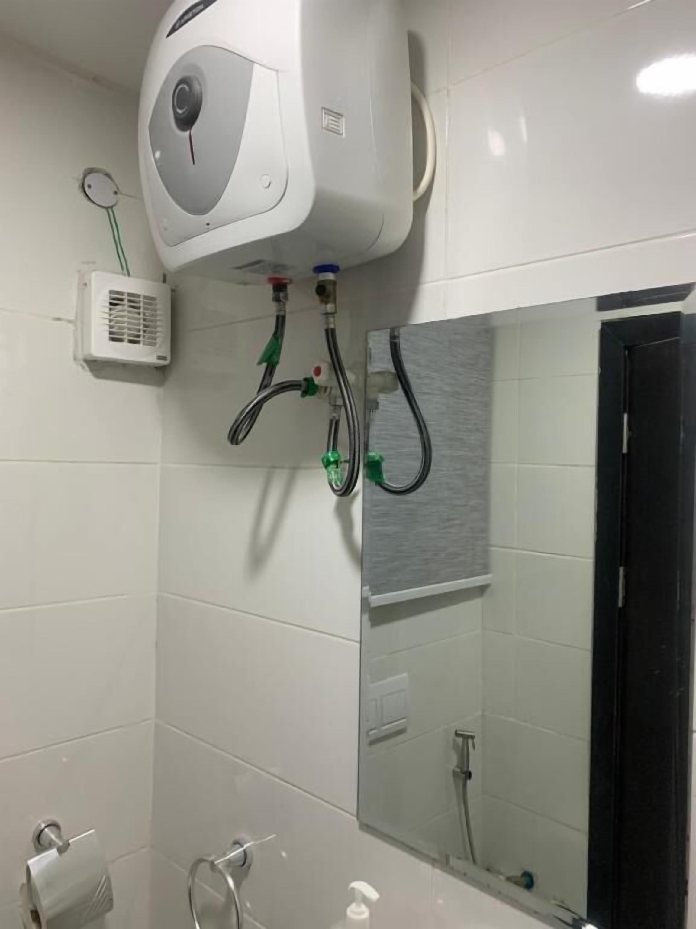 A bathroom with white tiles, a toilet paper holder, a hand dryer, and a mirror.