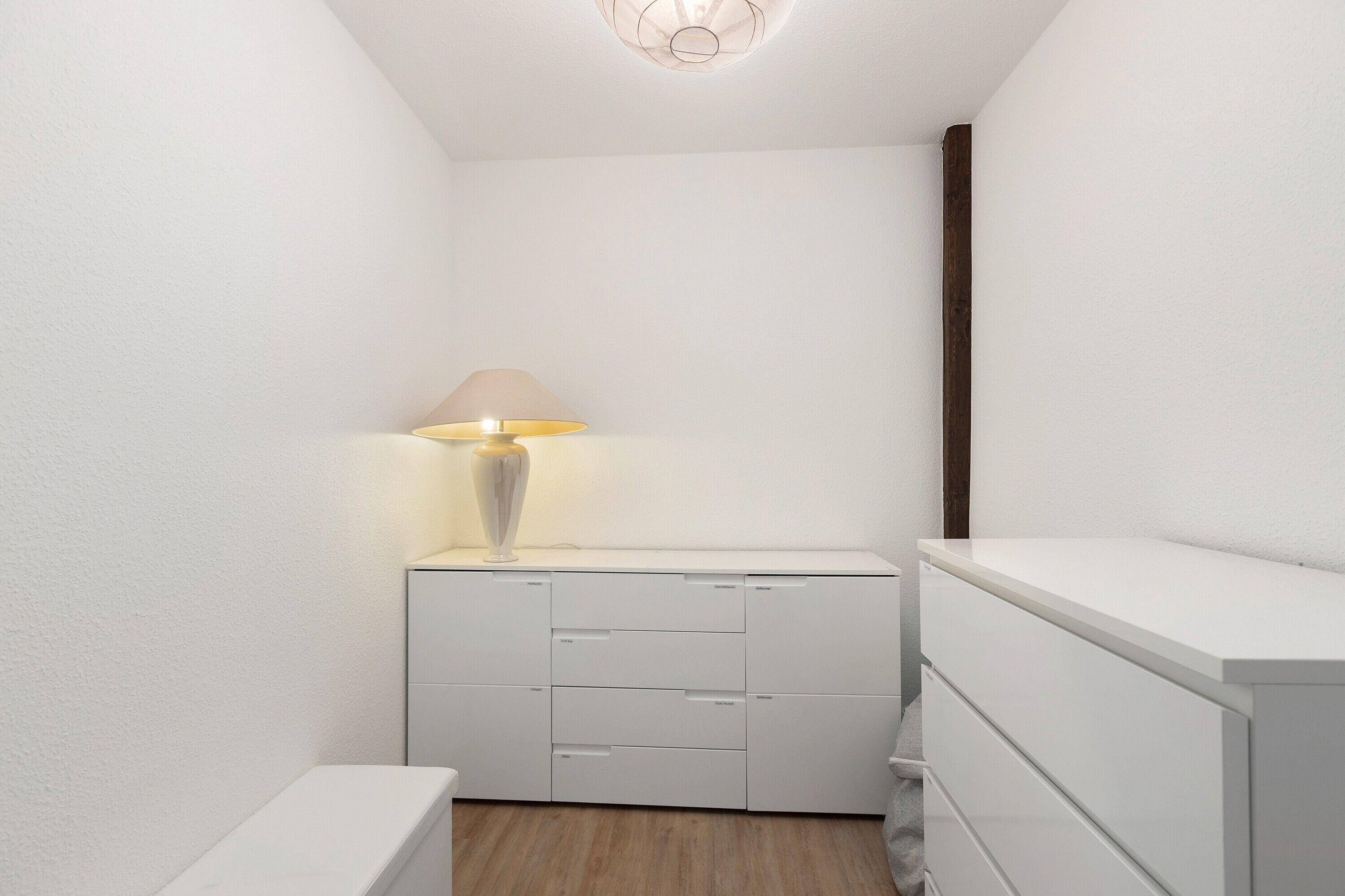 Un angolo di stanza con un armadietto bianco, una lampada e un pavimento in legno.
