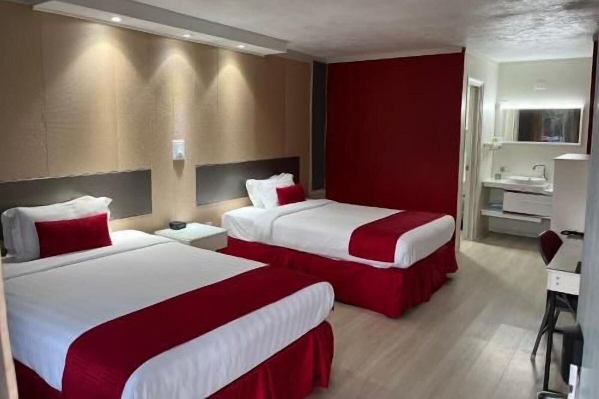 A hotel room with two beds, a desk, and a bathroom.