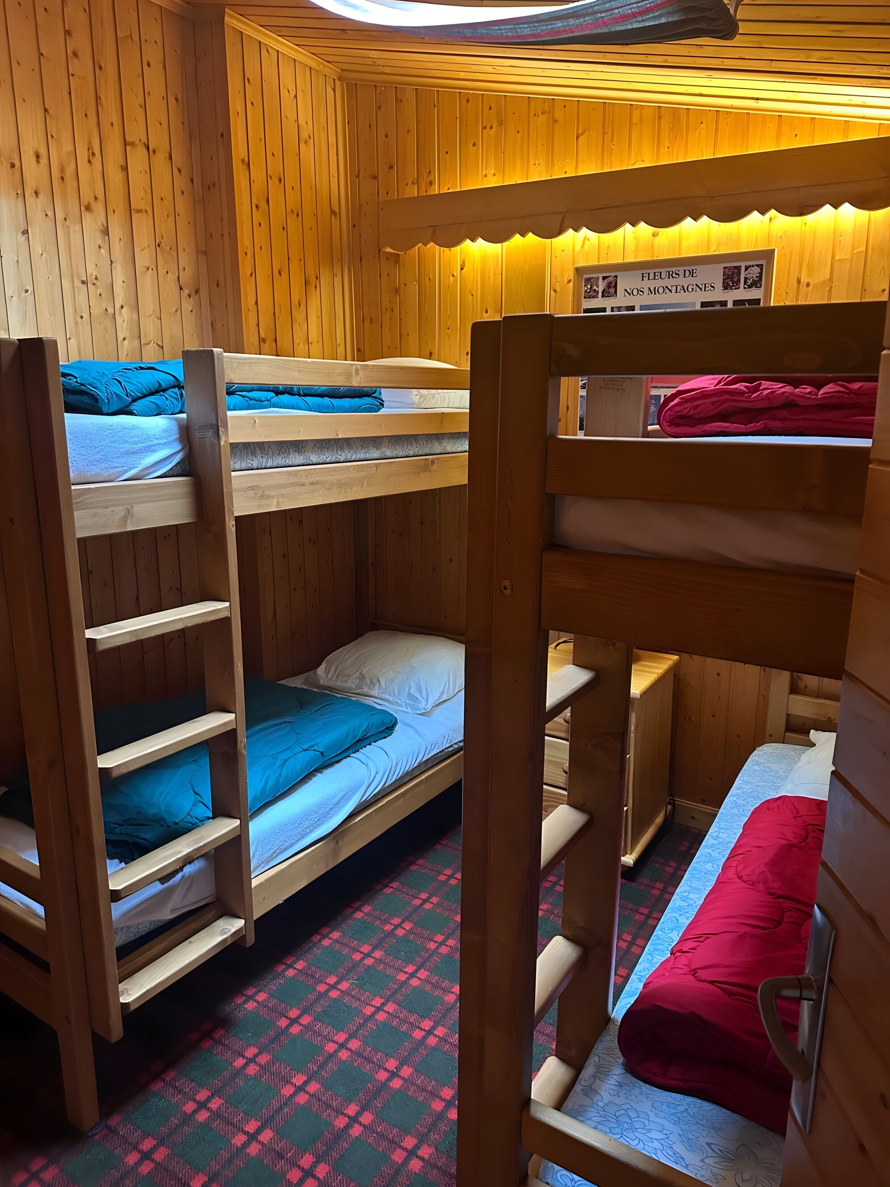 A wooden cabin with bunk beds, a plaid floor mat, and a sign indicating it's a mountain lodge.