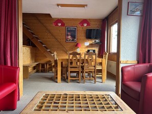 Ein Holzinterieur mit Essbereich, roten Ledersesseln, einem Fernseher und einer Treppe.