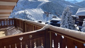Un balcón de madera con vistas a montañas nevadas y una estación de esquí.