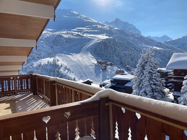 A wooden balcony with a view of snow-covered mountains and a ski resort.
