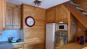 Una cocina de madera con un reloj, un refrigerador, un microondas y una estufa.