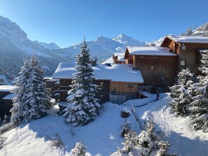 Un rifugio di montagna imbiancato dalla neve, con architettura in legno, circondato da alberi e montagne carichi di neve.