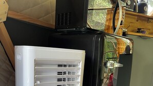 A compact kitchenette with a white appliance, a black appliance, and a wooden cabinet with a kettle. - Nature Dome & Jacuzzi at Blue Grass Ranch (Bischoffsheim)