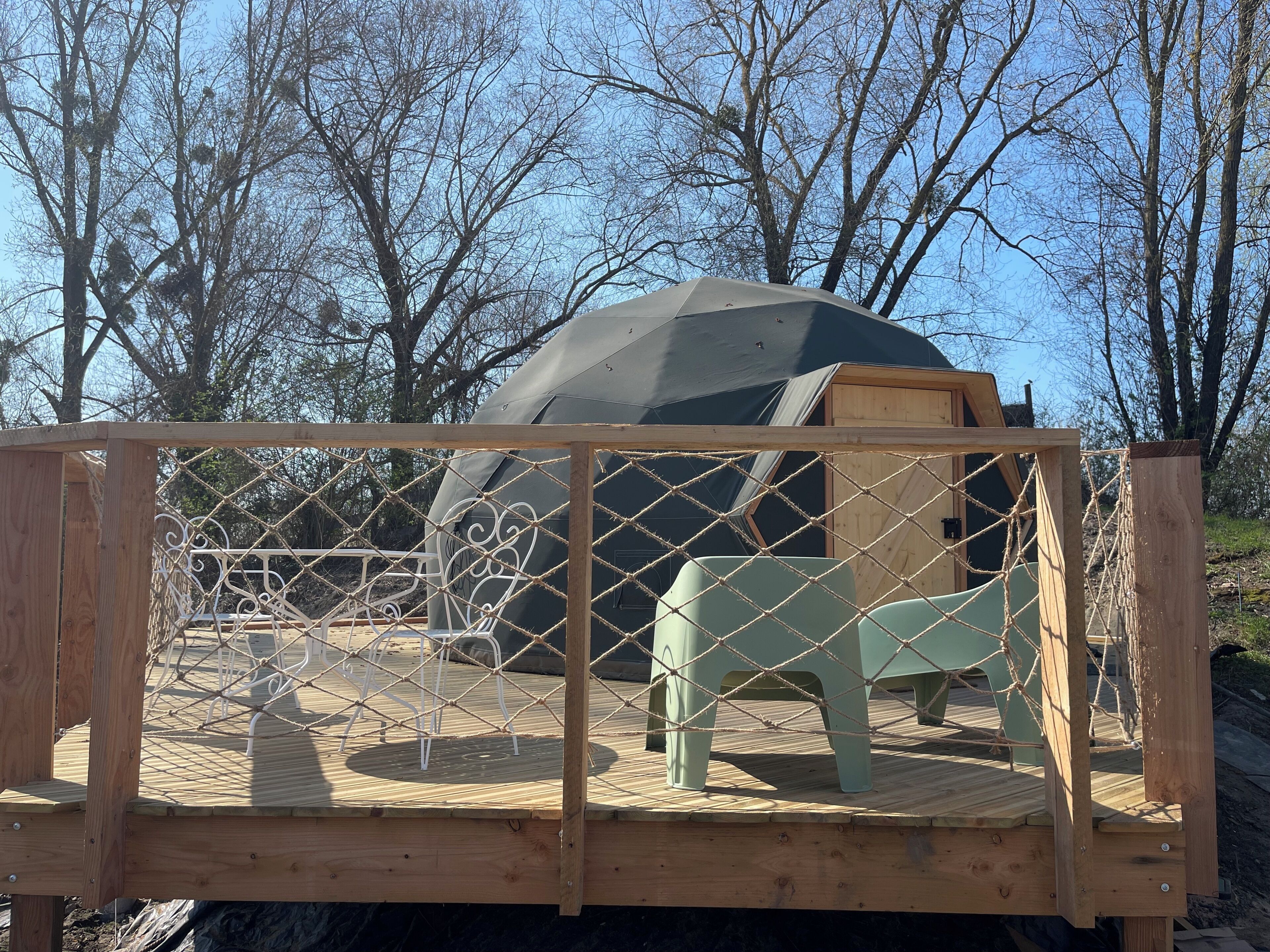 A geodesic dome structure with a wooden deck and a rope fence.