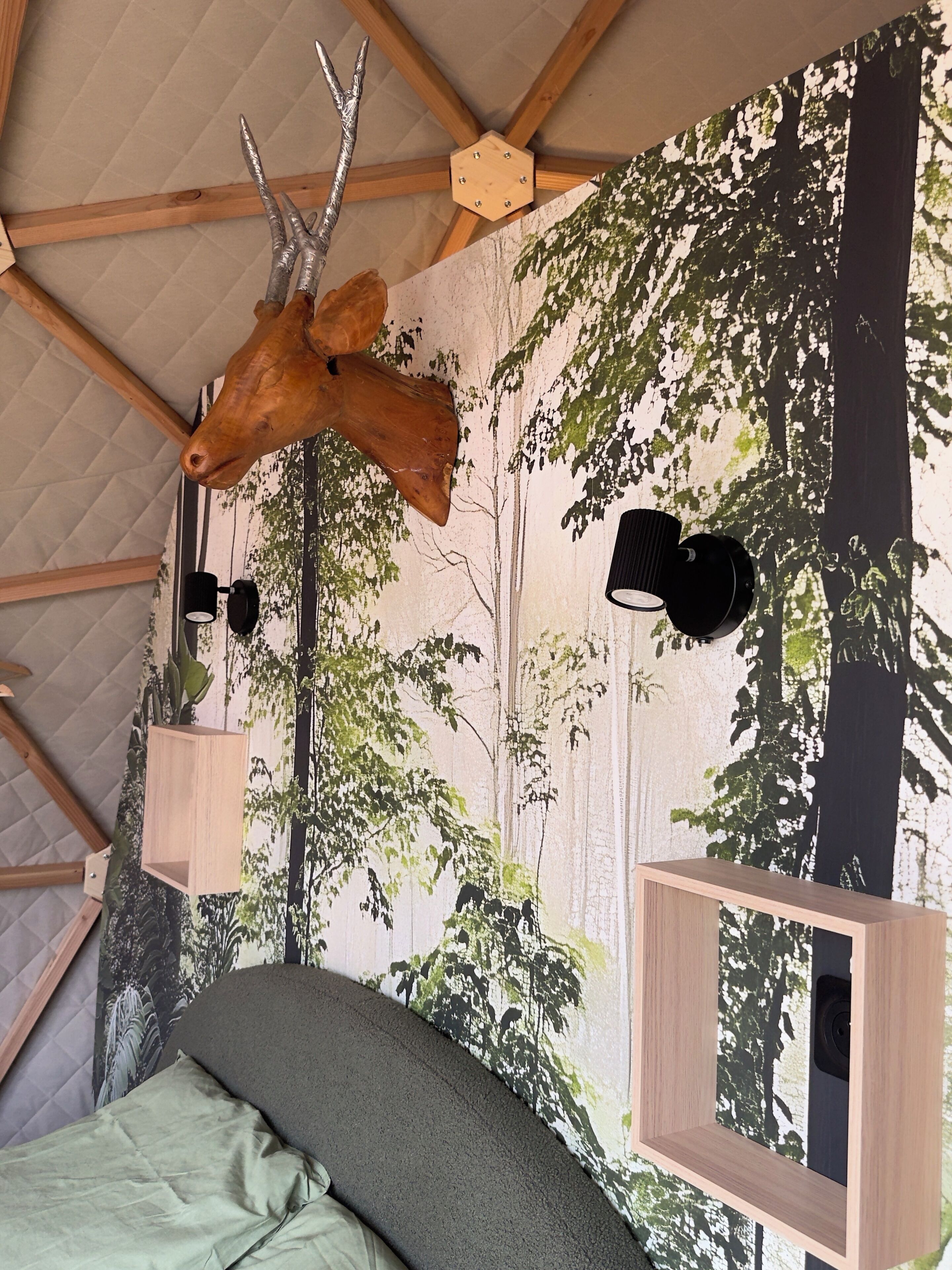 Ein Schlafzimmer mit Holzbalkendecke, einem großen Hirschgeweih an der Wand und einem Wandpapier mit Waldmotiv.