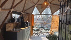 An interior of a geodesic dome with a kitchen area, dining table, chairs, and a hanging light fixture. - Nature Dome & Jacuzzi at Blue Grass Ranch (Bischoffsheim)