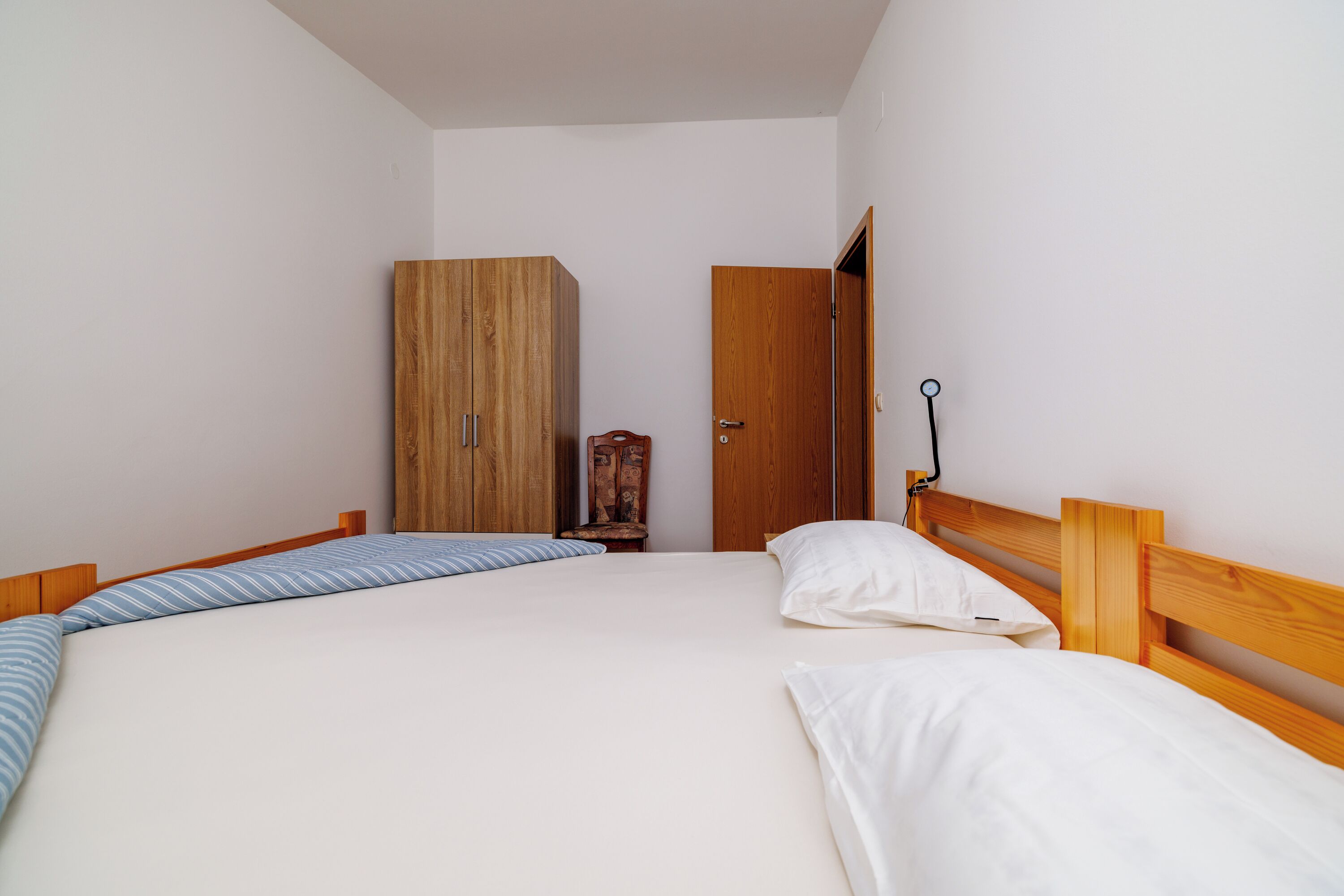 A bedroom with two beds, a wardrobe, a chair, and a door.