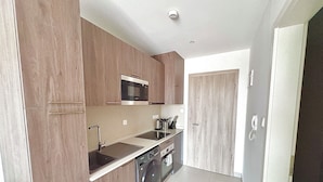 Una cocina compacta con armarios de madera, microondas, cafetera y lavadora.