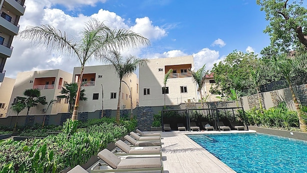 Un área junto a la piscina con sillones de descanso, una pileta y edificios al fondo.