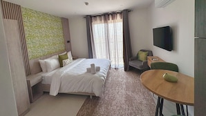Una habitación de hotel con cama, escritorio, silla, televisor y ventana con cortinas.