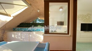 A modern kitchen with a large window, a dining area with blue cushioned chairs, and a television on the wall. - Bay beach apartment (Santa Teresa Gallura)