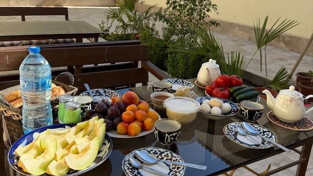 A glass-top table with various food items and a water bottle on a patio. - ORIENT HOUSE  (Bukhara)