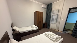 A hotel room with two beds, a wardrobe, an air conditioning unit, and a view of the outside through a window. - ORIENT HOUSE  (Bukhara)