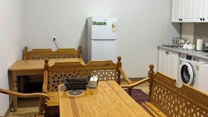 A compact kitchen with a refrigerator, washing machine, and wooden furniture. - ORIENT HOUSE  (Bukhara)