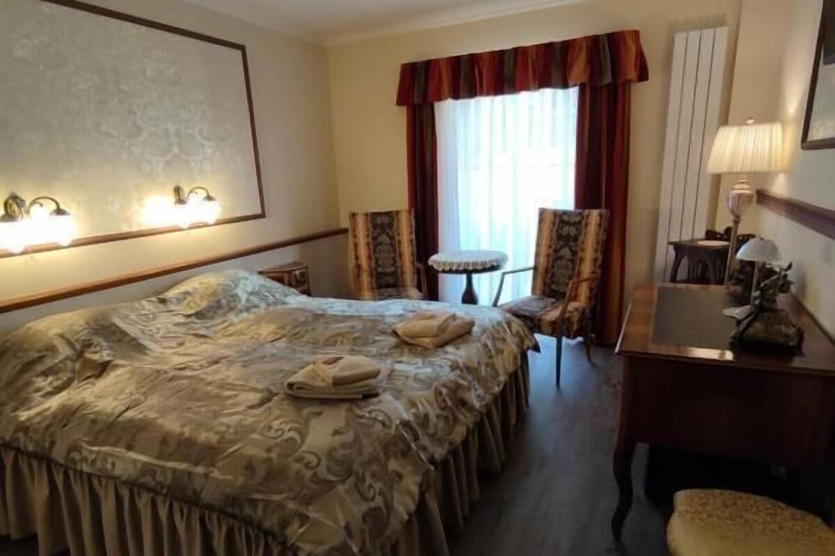 A hotel room with a large bed, two armchairs, a small table, and a desk with a lamp.
