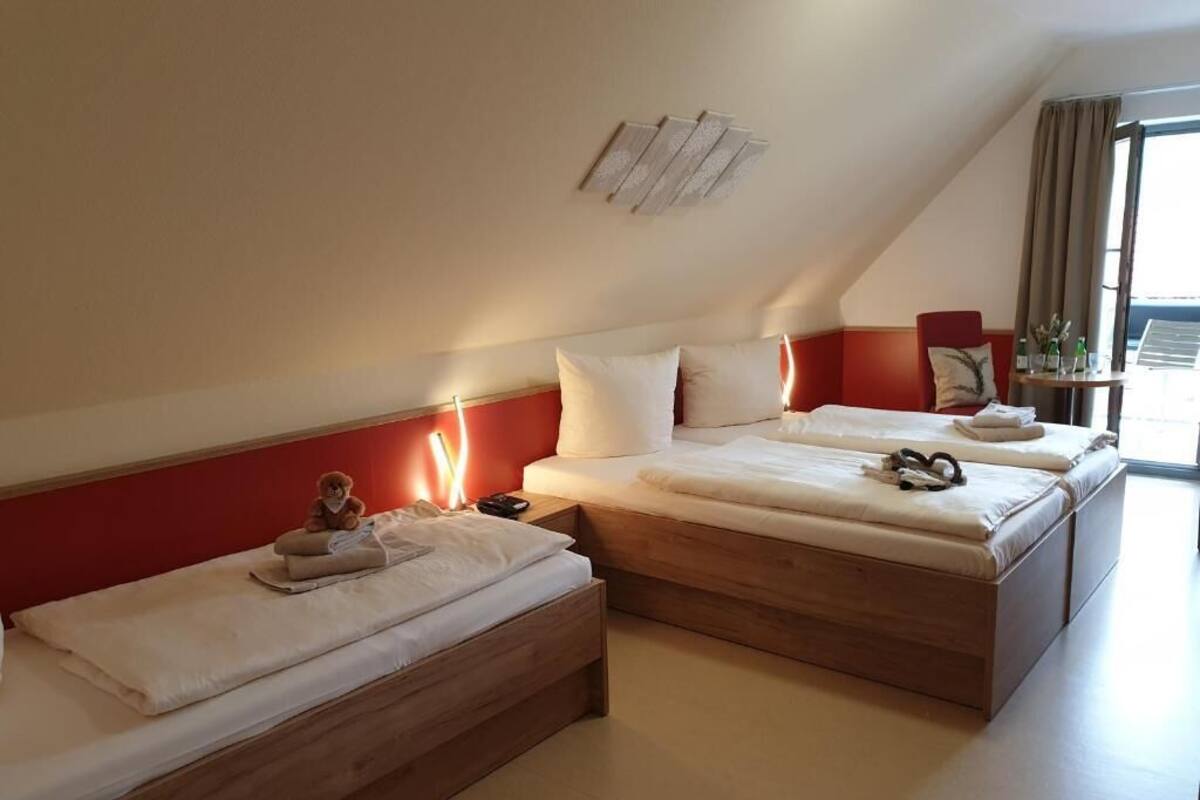 A hotel room with two beds, a red accent wall, a small table with toiletries, and a window with curtains.