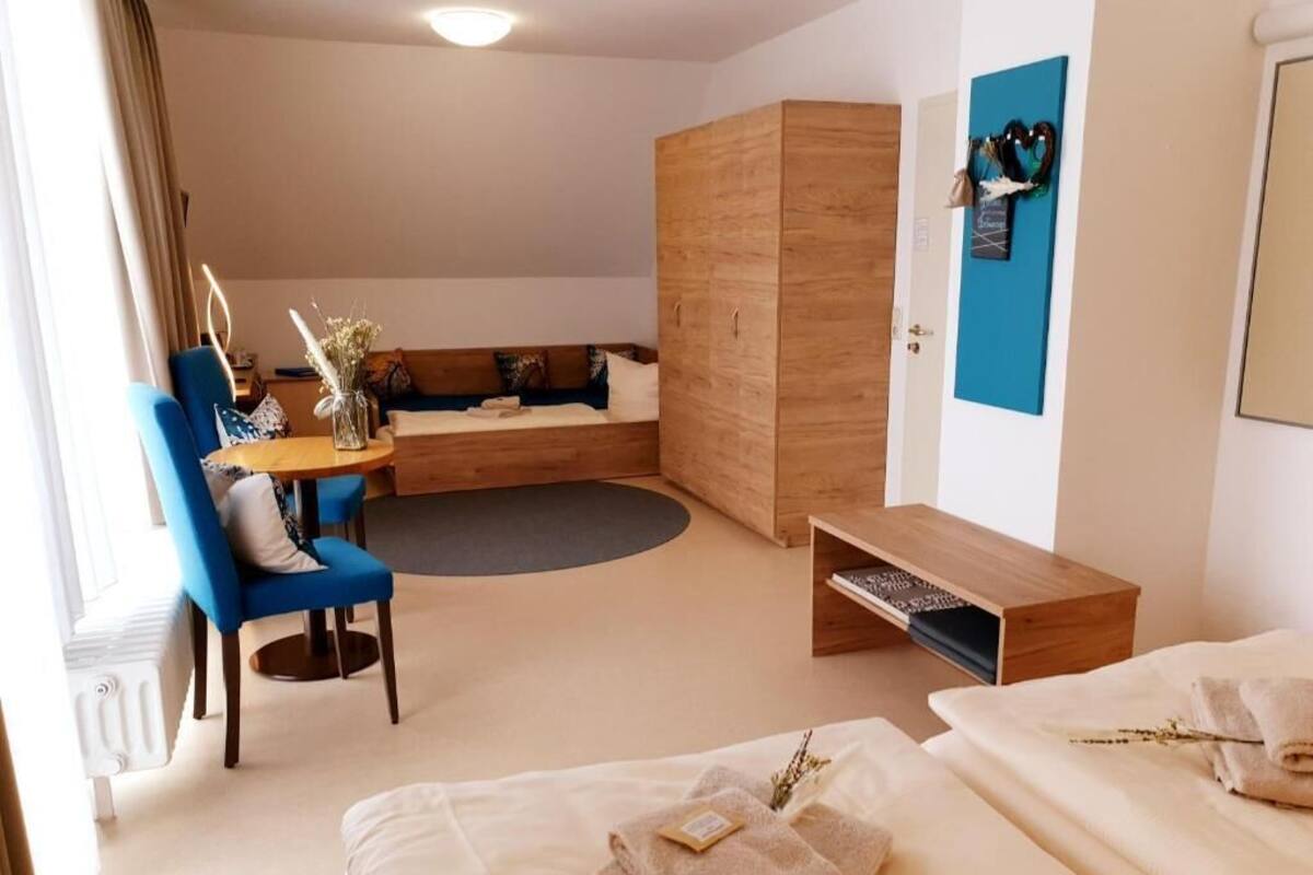 A hotel room with a bed, a seating area with a table, a wardrobe, and a blue wall.