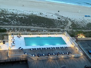 Vue aérienne d’un hôtel situé en bord de mer, avec une grande piscine, des chaises longues et une terrasse en bois.