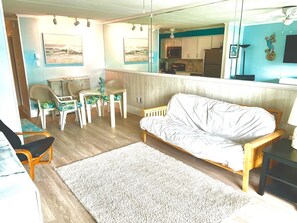 A living room with a sofa, chairs, a coffee table, a rug, and a kitchen area visible through a glass partition. - Lovely one Bedroom ocean block closer to Downtown Ocean City (Ocean City)