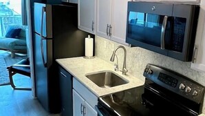 Une cuisine avec des meubles blancs, une cuisinière noire, un évier et un four à micro-ondes.