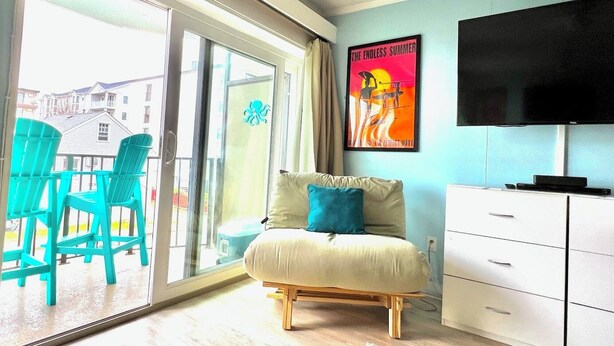 Une chambre à coucher avec un lit, une télévision, une porte-fenêtre coulissante et une affiche accrochée au mur.