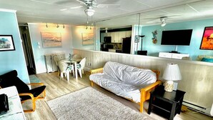 Un salon moderne comprenant un canapé, une table à manger avec des chaises, un téléviseur et un ventilateur de plafond.