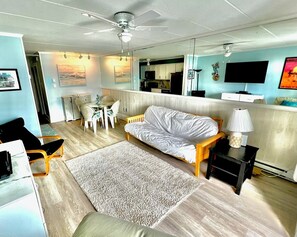 A modern living room with a sofa, a dining table with chairs, a TV, and a ceiling fan. - Lovely one Bedroom ocean block closer to Downtown Ocean City (Ocean City)