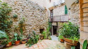 Une cour bordée de murs en pierre, agrémentée de plantes en pot et dotée d’un sol carrelé.