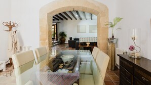 Un espace repas comprenant une table en verre, des chaises, une arche en pierre, un canapé et une plante en pot.