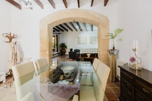 A dining area with a glass table, chairs, a stone archway, a sofa, and a potted plant. - A Charming terraced house in the heart of Pollensa, in the Escaleras del Calvario area, with a large swimming pool. (Pollensa / Pollença)
