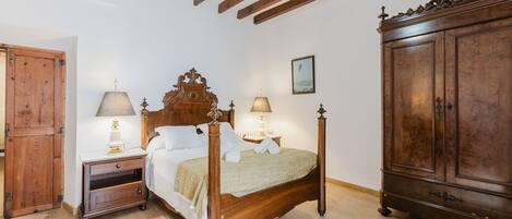 A bedroom with a wooden bed, two bedside tables with lamps, a wardrobe, and a ceiling with exposed beams.