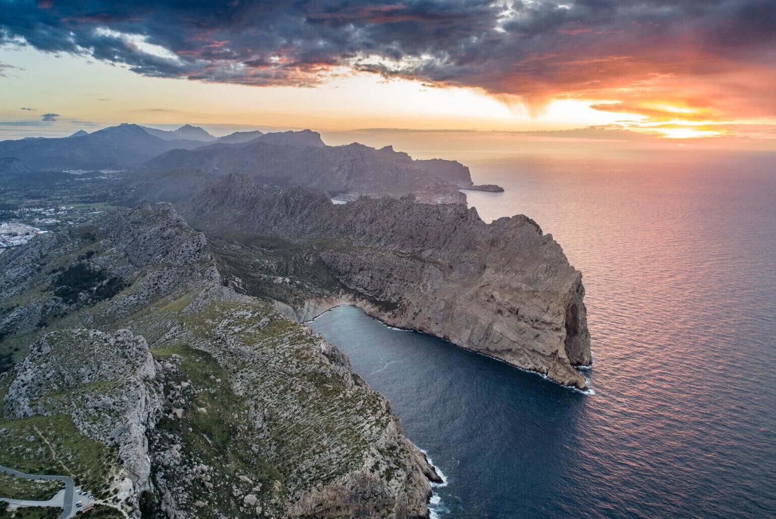 Un paisaje costero con acantilados escarpados, un estrecho canal de agua y una vista distante de montañas.