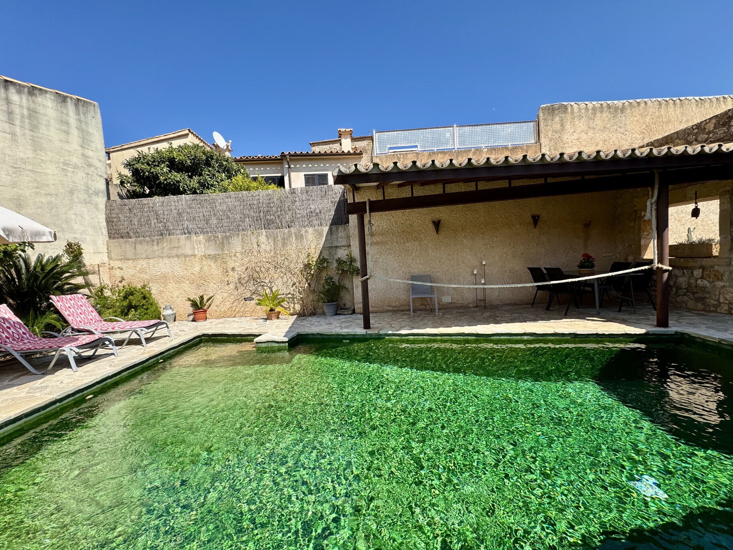 A clear pool with lounge chairs, a covered seating area, and a stone wall.