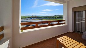 Een balkon met uitzicht op een meer en bergen, een houten bankje en een schuifdeur.