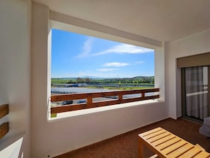 A balcony with a view of a lake and mountains, a wooden bench, and a sliding glass door. - KriMni Confort Feet in the water, 25 min from Tangier (Asilah)