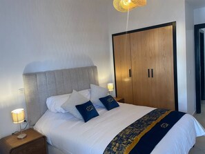 Ein ordentlich bezogenes Bett mit weißer und dunkelblauer Bettdecke, zwei Kissen und einer Nachttischlampe.