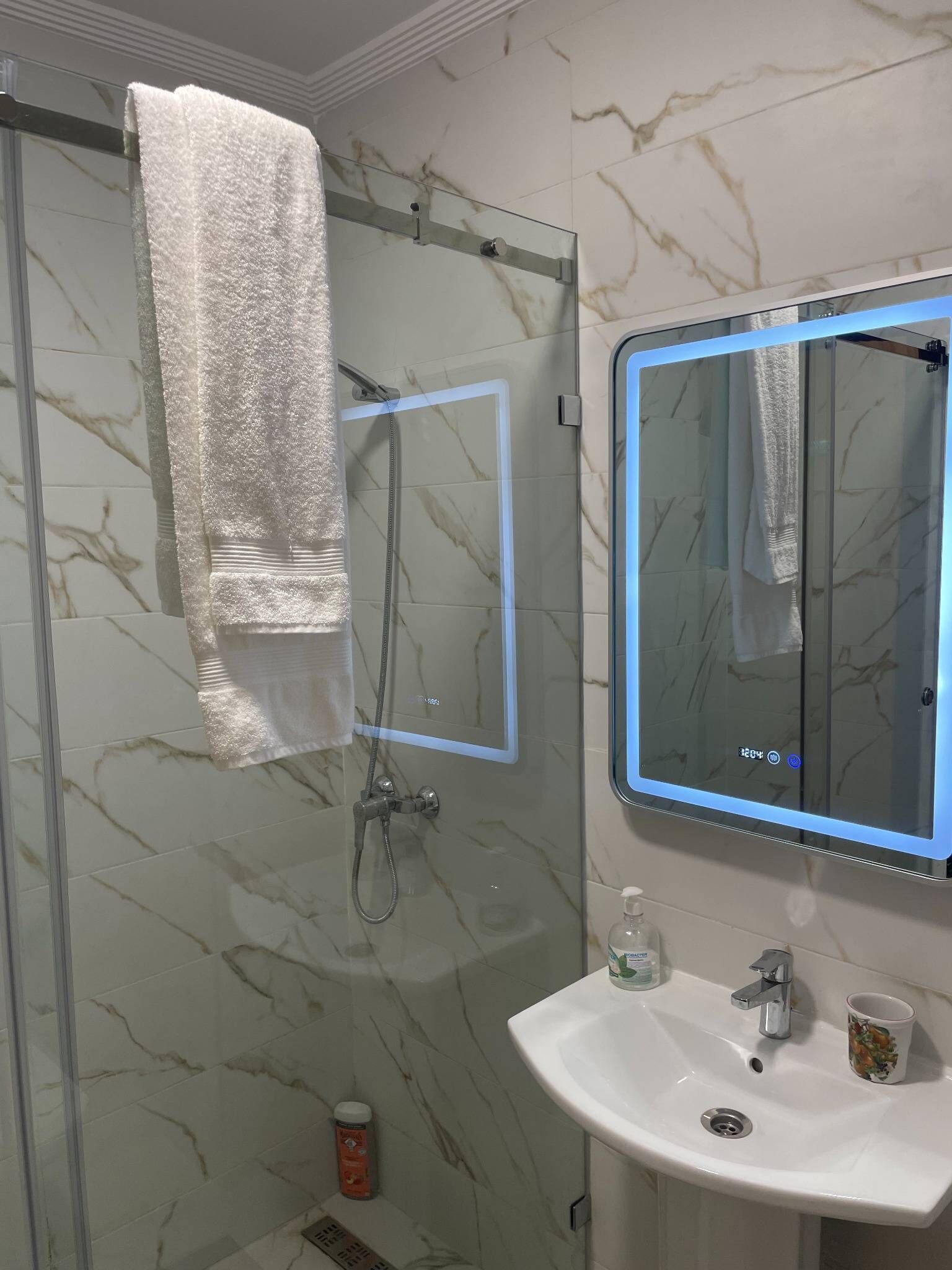 Une salle de bain avec une douche à parois de verre, un lavabo blanc, un miroir avec un cadre bleu et une serviette suspendue à un porte-serviettes.